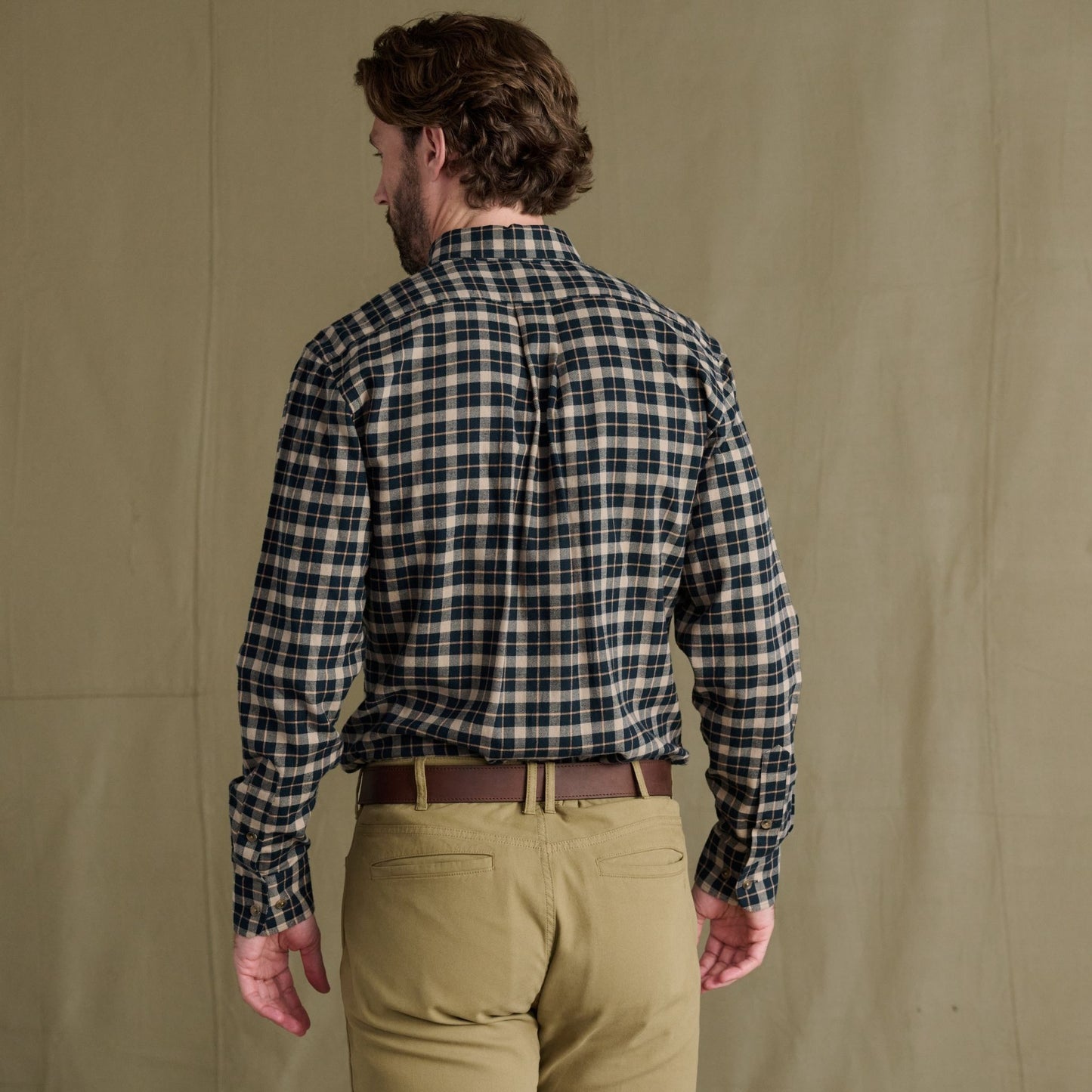 Man facing away in a Tom Beckbe Dixon Brushed Cotton Twill Shirt with khaki pants before a plain beige background.