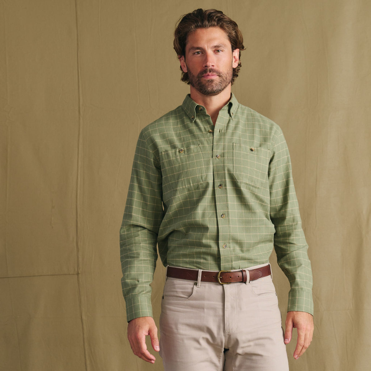 Man in a Tom Beckbe Dixon Brushed Cotton Twill Shirt, brown belt, and beige pants stands by a plain tan backdrop.
