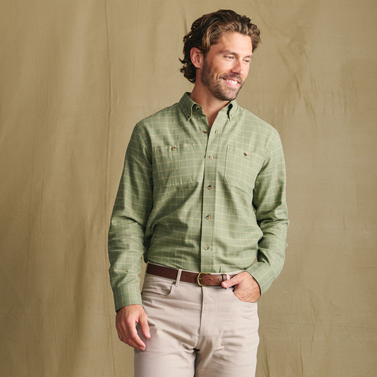 Man wears Tom Beckbe Dixon Brushed Cotton Twill Shirt in green plaid, smiling against a plain tan backdrop.