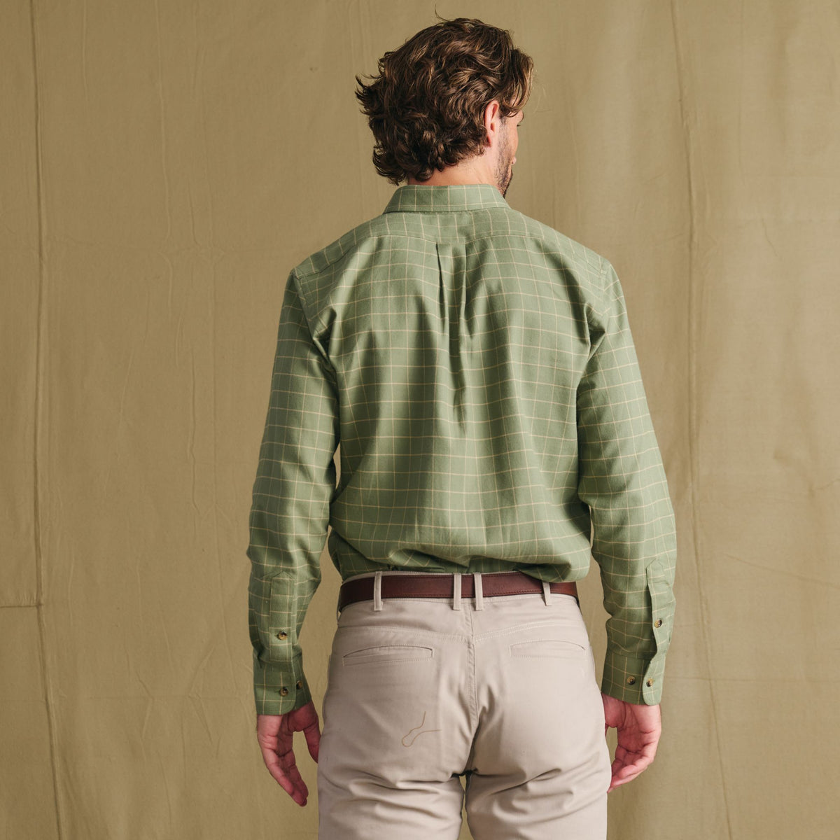 Man facing away in Tom Beckbe Dixon Brushed Cotton Twill Shirt, green check, and beige pants on a light brown backdrop.