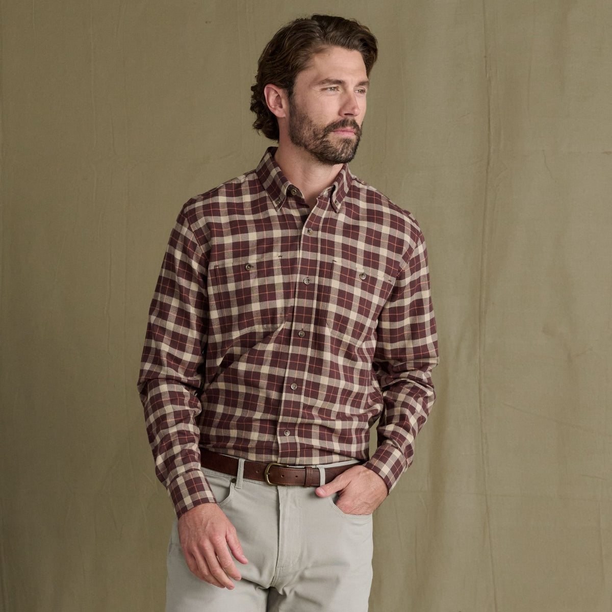 Man wears Tom Beckbe’s Dixon Brushed Cotton Twill Shirt and light khaki pants, posed before an olive-green backdrop.