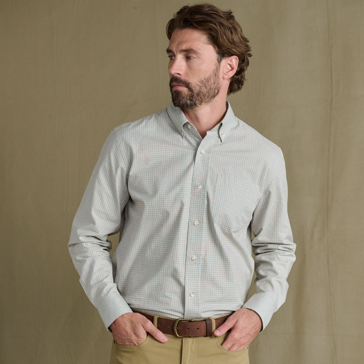 Bearded man in Tom Beckbe Ensley Pinpoint Oxford Shirt and khaki pants stands before a plain beige background.
