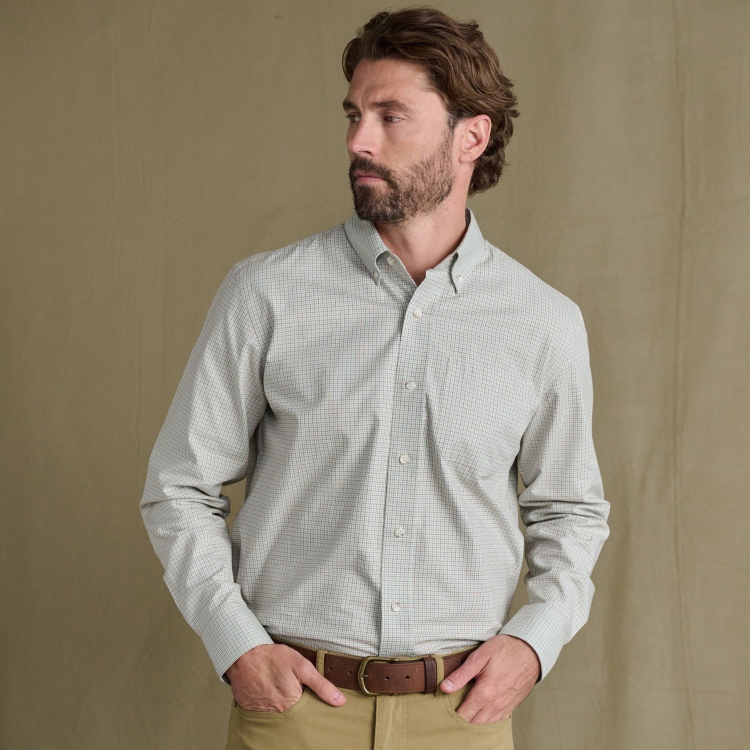 Bearded man in Tom Beckbe Ensley Pinpoint Oxford Shirt and khaki pants stands before a plain beige background.