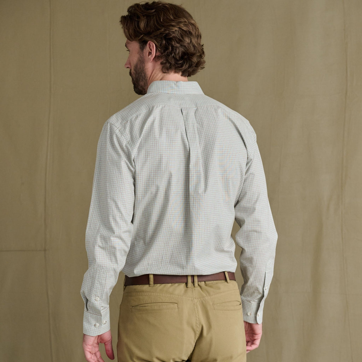 Man in a Tom Beckbe Ensley Pinpoint Oxford Shirt and khakis stands facing away before a plain beige background.
