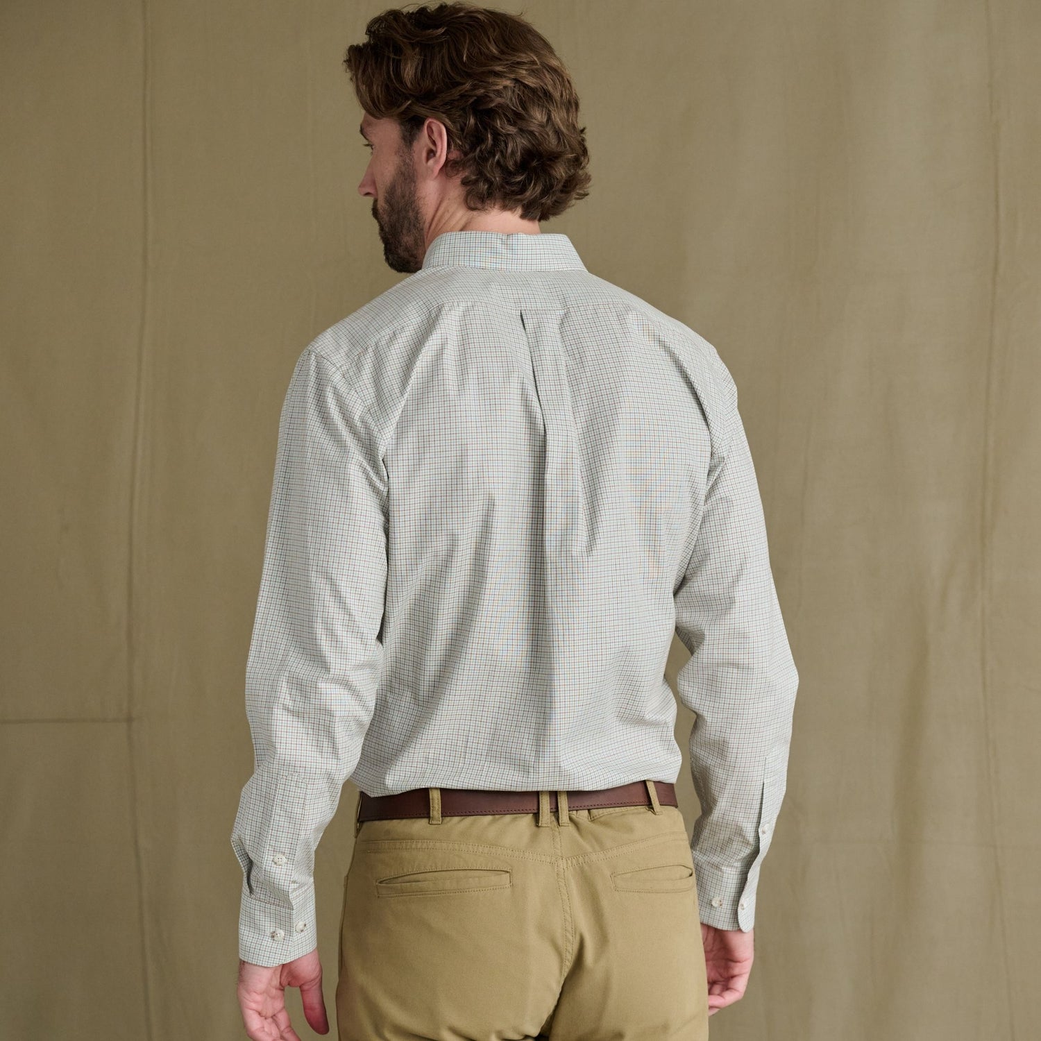 Man in a Tom Beckbe Ensley Pinpoint Oxford Shirt and khakis stands facing away before a plain beige background.