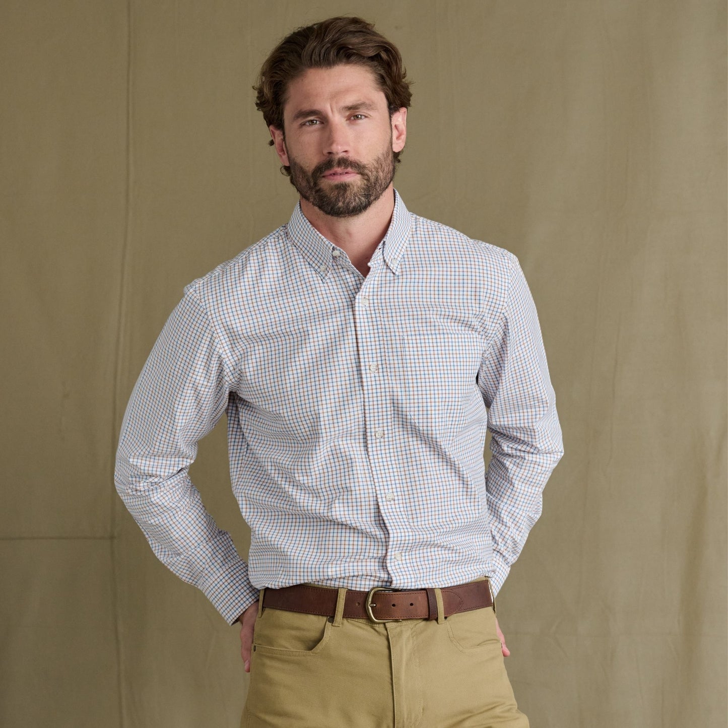 Man with brown hair and beard wears a Tom Beckbe Ensley Pinpoint Oxford Shirt and khaki pants before a plain background.