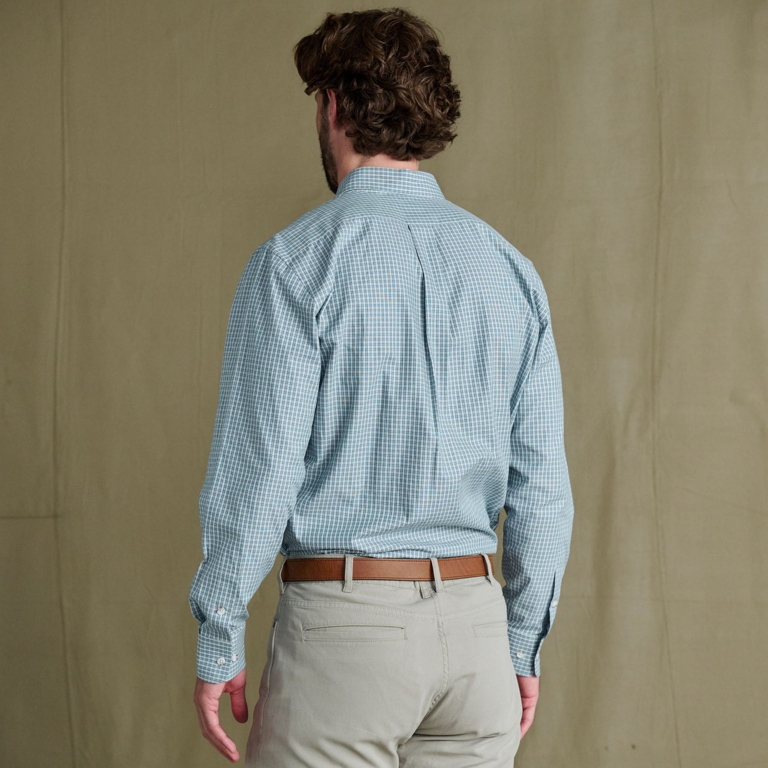 Man facing away in a Tom Beckbe Ensley Pinpoint Oxford Shirt, khaki pants, and brown belt against beige background.