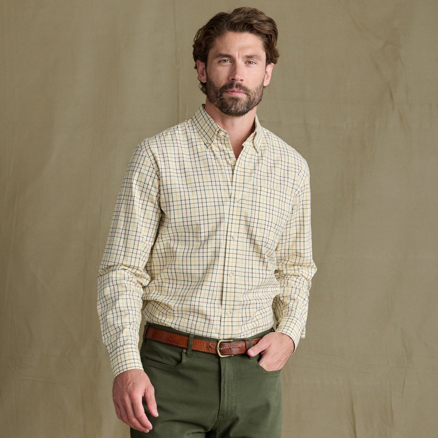 Man wears Tom Beckbe Ensley Pinpoint Oxford Shirt and green pants, standing before a plain khaki background.
