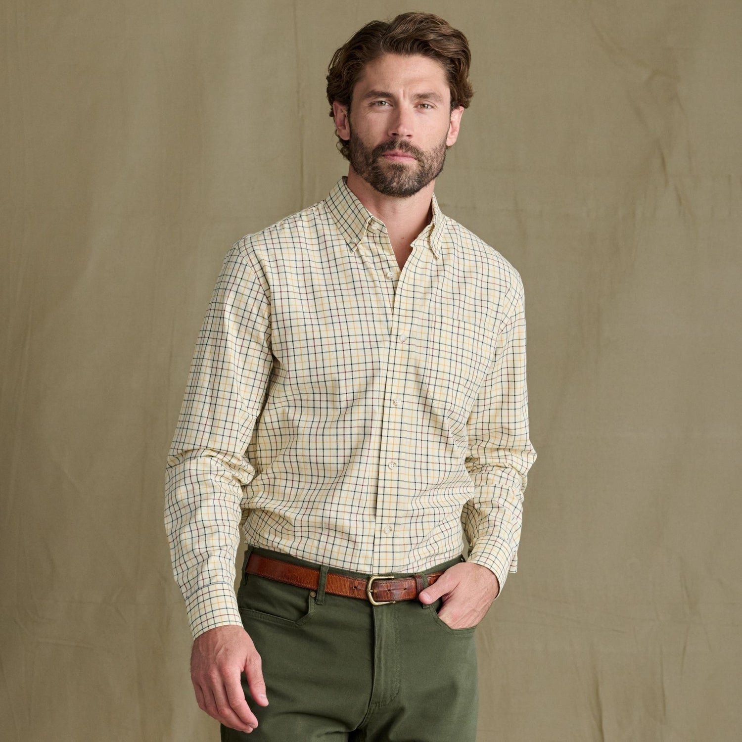 Man wears Tom Beckbe Ensley Pinpoint Oxford Shirt and green pants, standing before a plain khaki background.