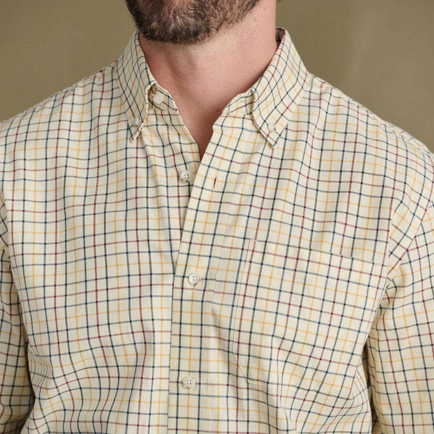 Man wears Tom Beckbe Ensley Pinpoint Oxford, plaid with red, yellow, blue lines; shown neck to chest.