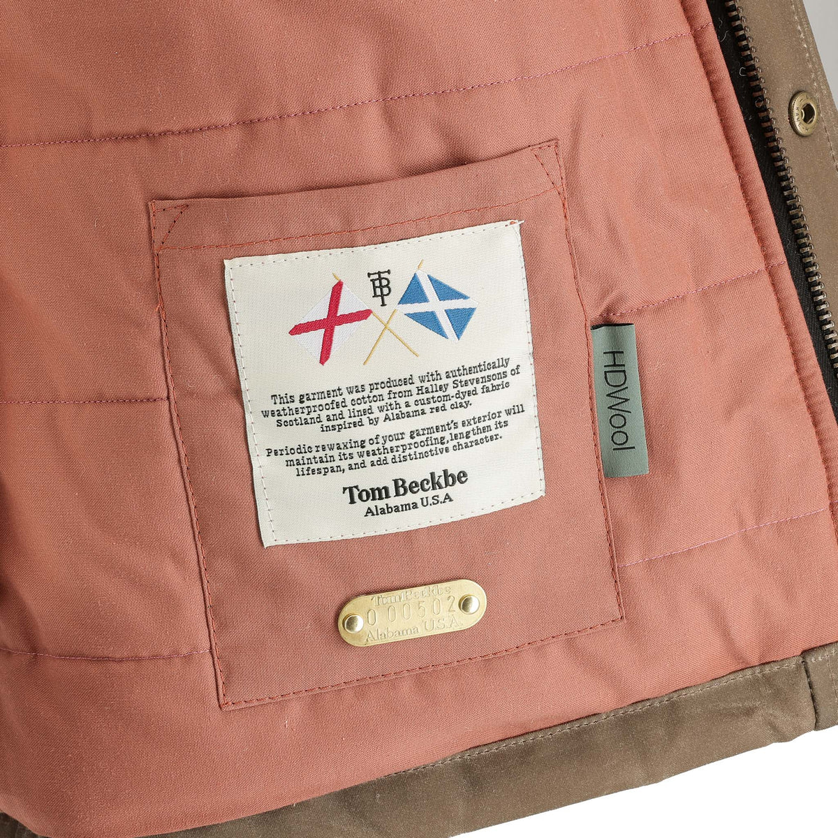A close-up of the Tom Beckbe Fowler Jacket’s interior pocket, showing fabric labels and a metal tag.