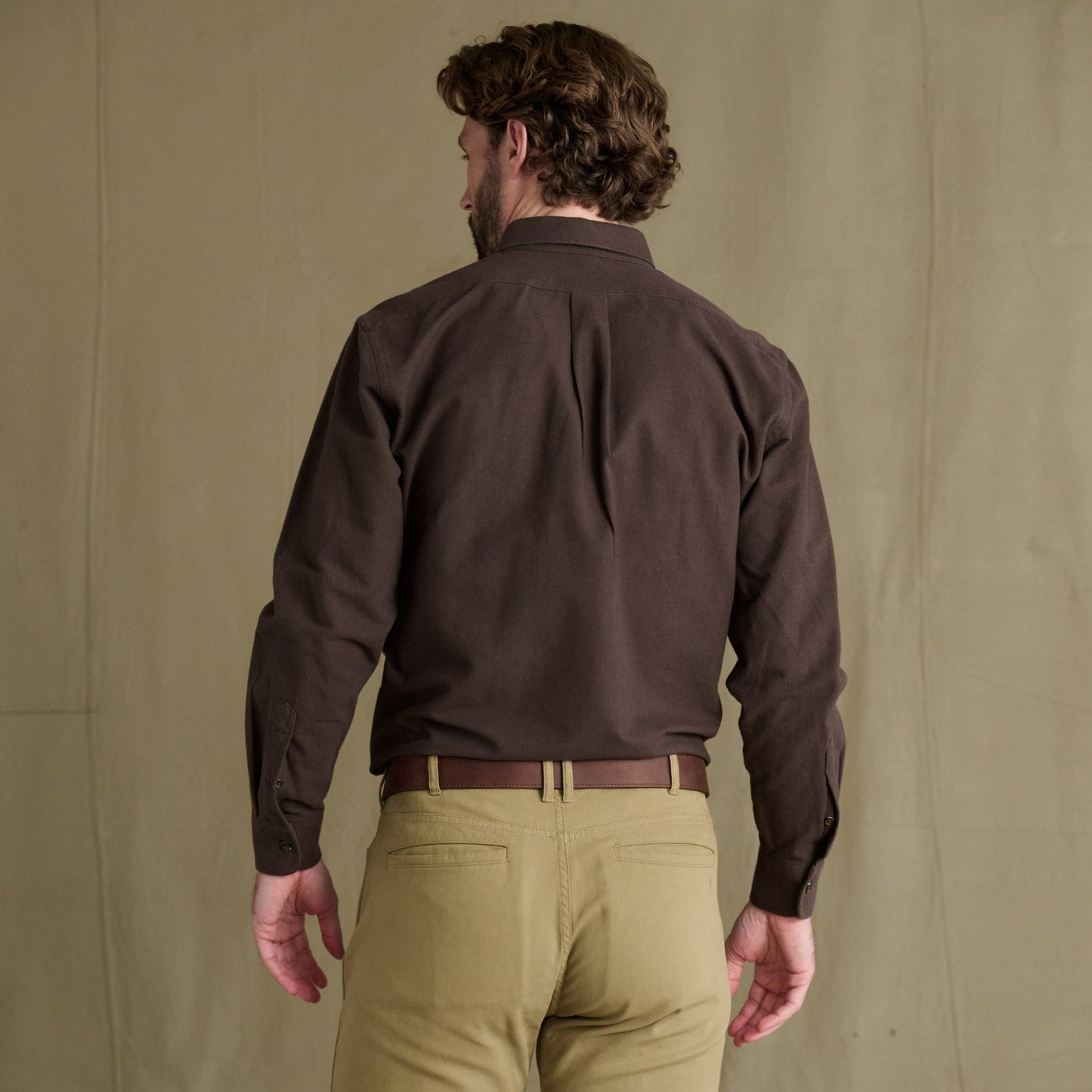 Man faces away in Tom Beckbe Hartwell Moleskin Shirt and tan pants before heritage waterfowl apparel backdrop.