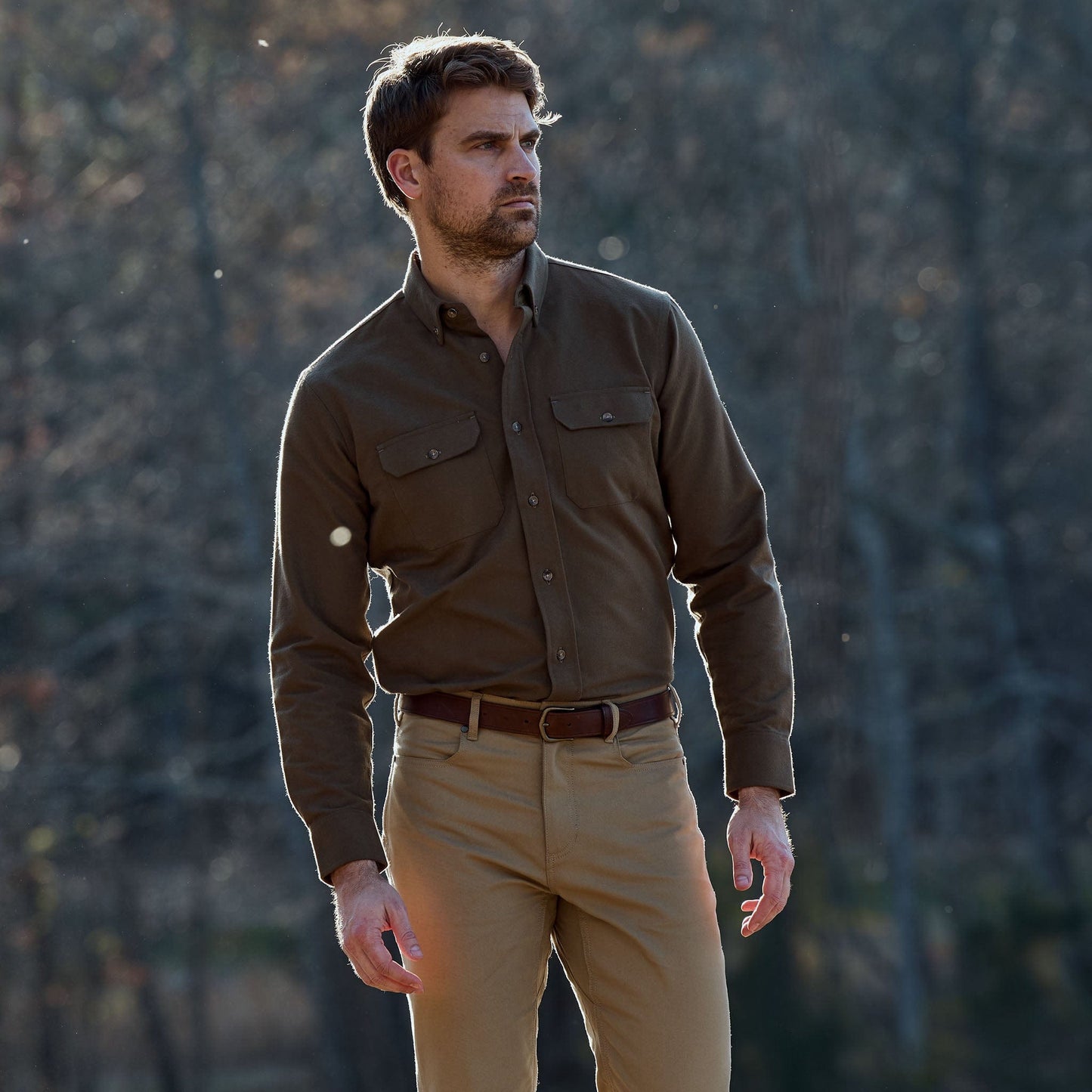 A man stands outdoors in a Tom Beckbe Hartwell Moleskin Shirt and tan pants, trees blurred in the background.