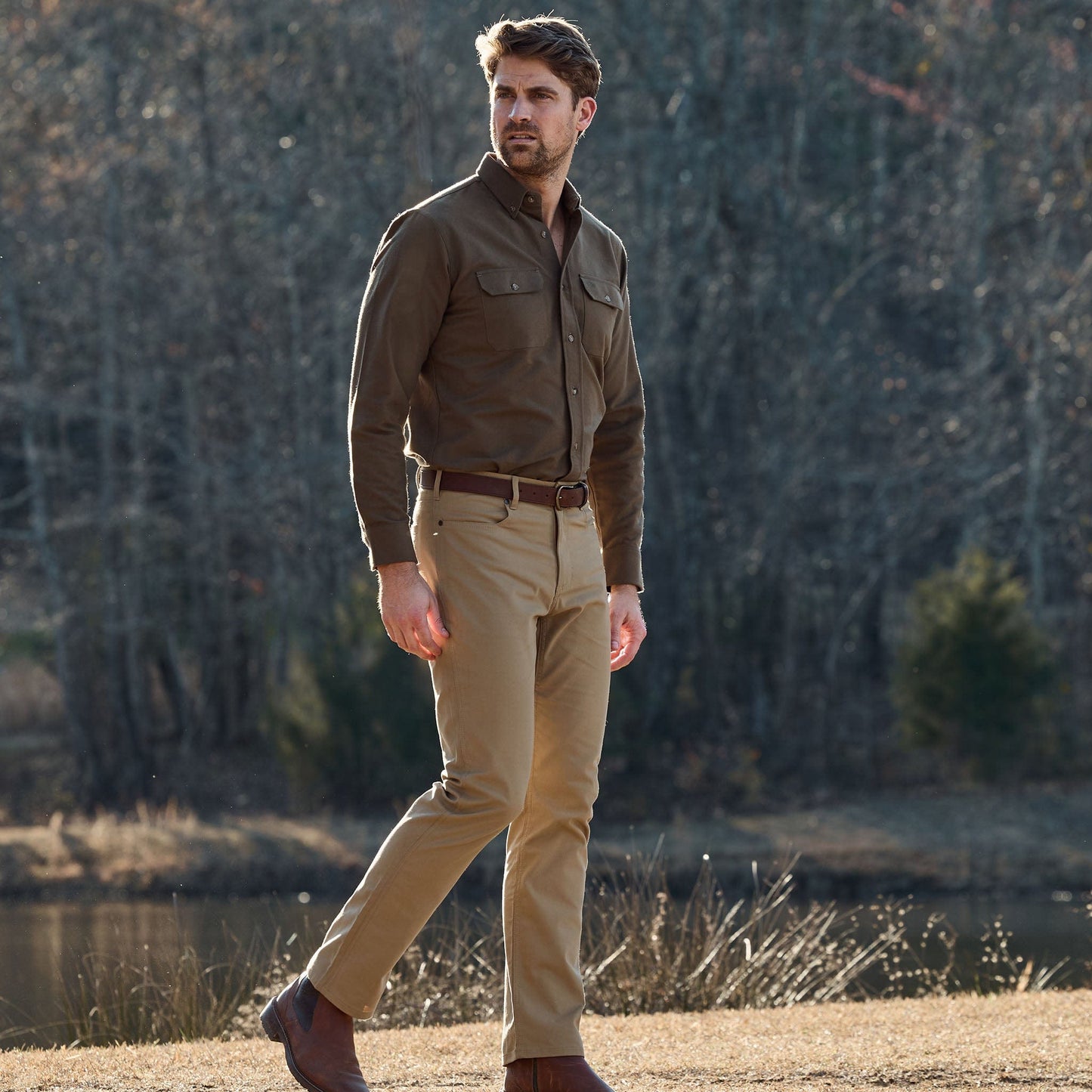 A man in a Tom Beckbe Hartwell Moleskin Shirt stands outdoors near trees and a pond.