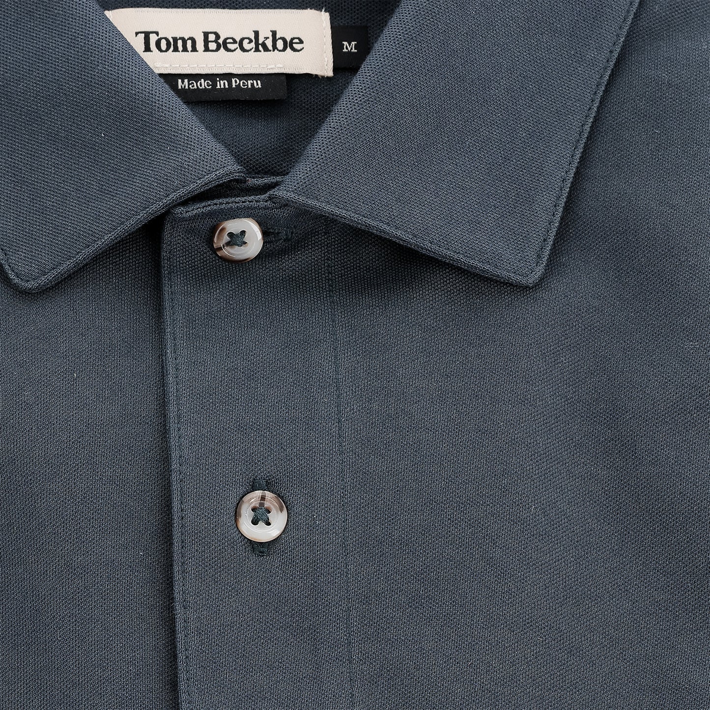 Close-up of a dark blue Hutton Performance Polo by Tom Beckbe, size M, with buttons and "Made in Peru" label.