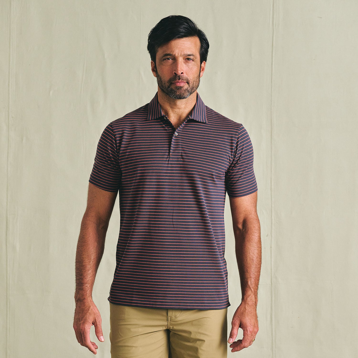 Man wearing the Tom Beckbe Hutton Performance Polo and khaki pants, standing against a plain light background.