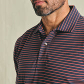 Man wearing Tom Beckbe Hutton Performance Polo in navy blue/red stripes, shown shoulders up against a plain background.