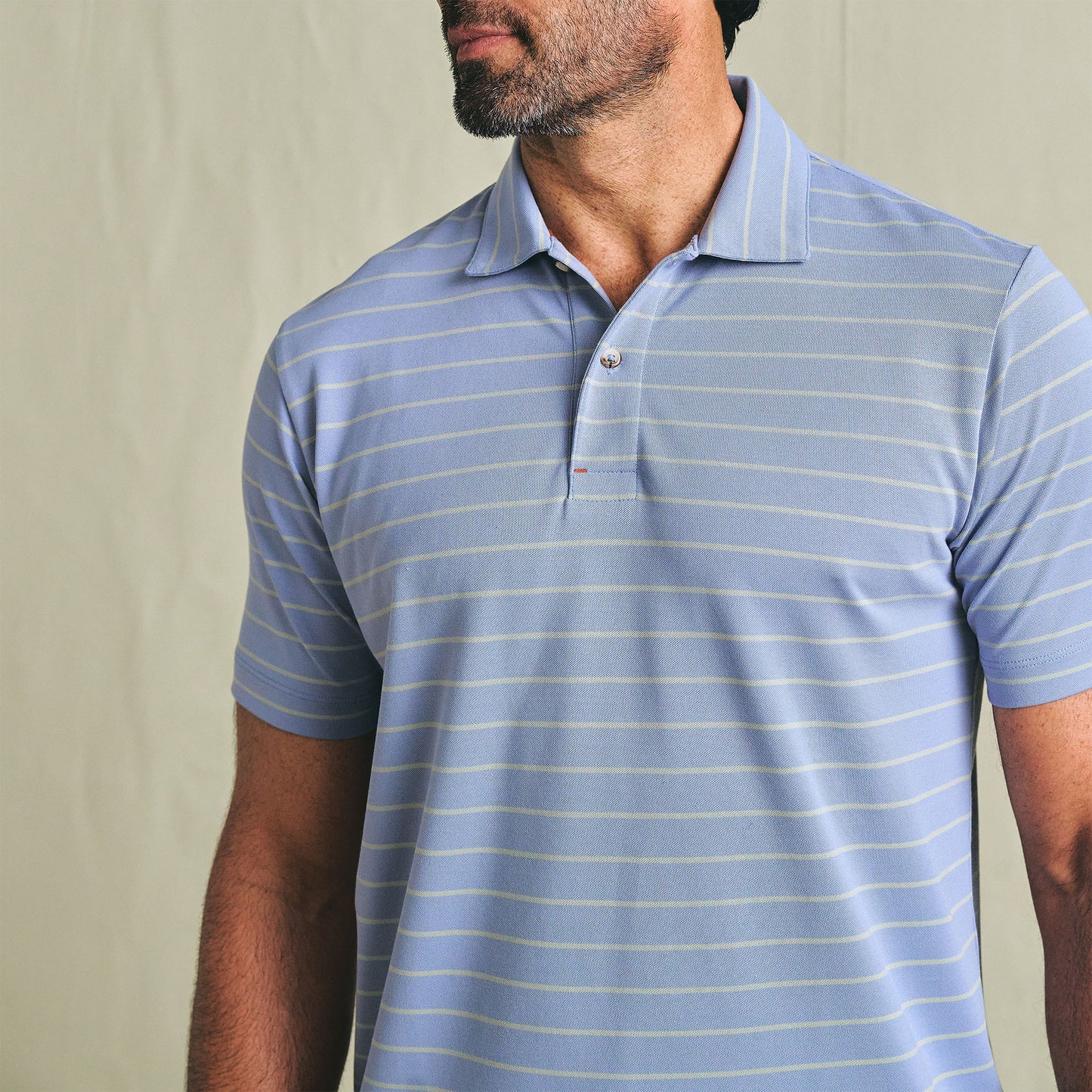 Man wearing the Tom Beckbe Hutton Performance Polo in light blue with thin white stripes, shown shoulders up.