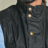 Close-up of a person wearing the Tom Beckbe Kinsman Vest with brass snaps over a light blue shirt.