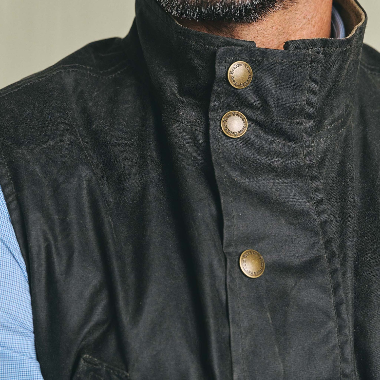 Close-up of a person wearing the Tom Beckbe Kinsman Vest with brass snaps over a light blue shirt.
