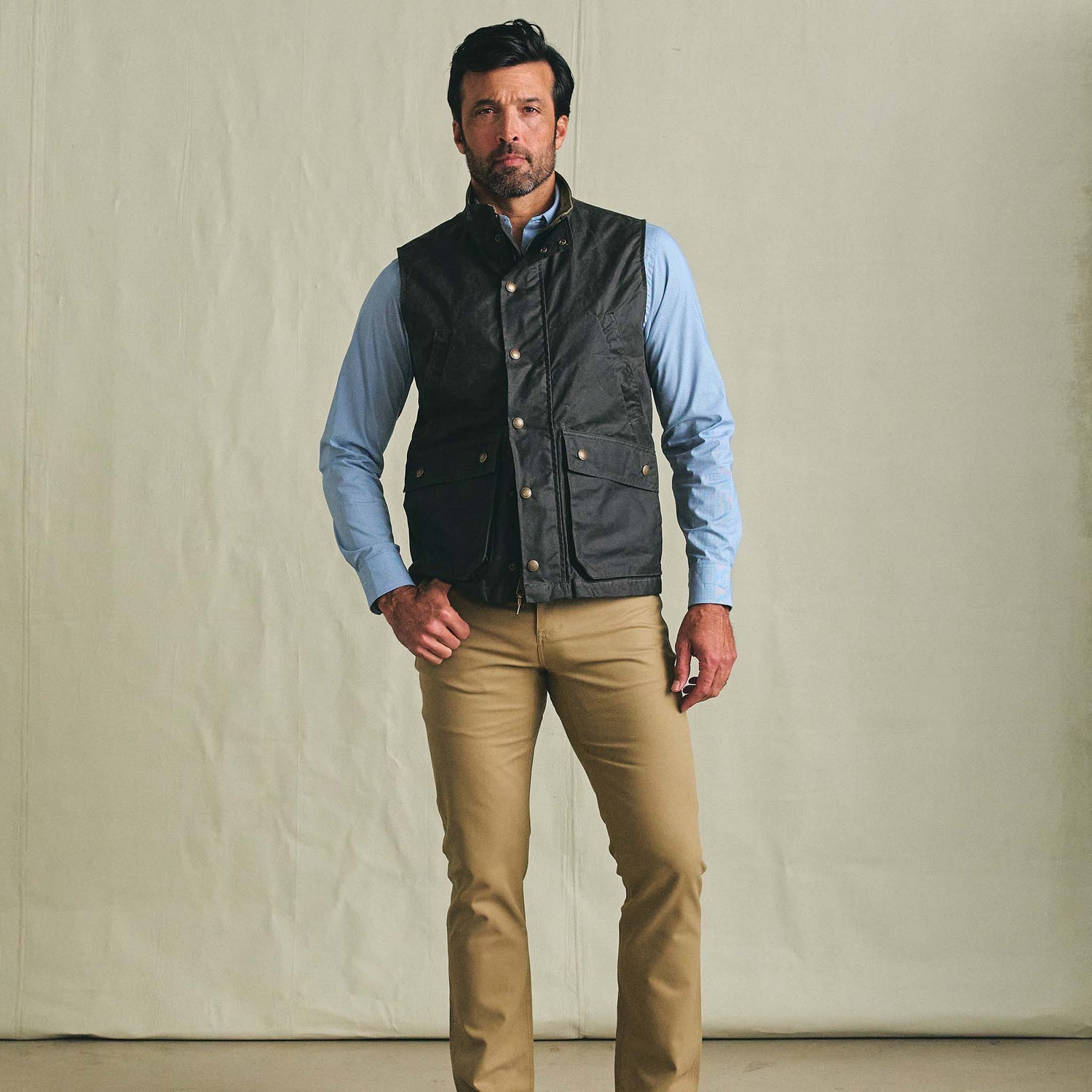 Man wears Tom Beckbe Kinsman Vest over a blue shirt and tan pants, standing against a plain background.