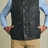 Person wearing the Tom Beckbe Kinsman Vest over a light blue shirt and tan pants, hands in vest pockets.