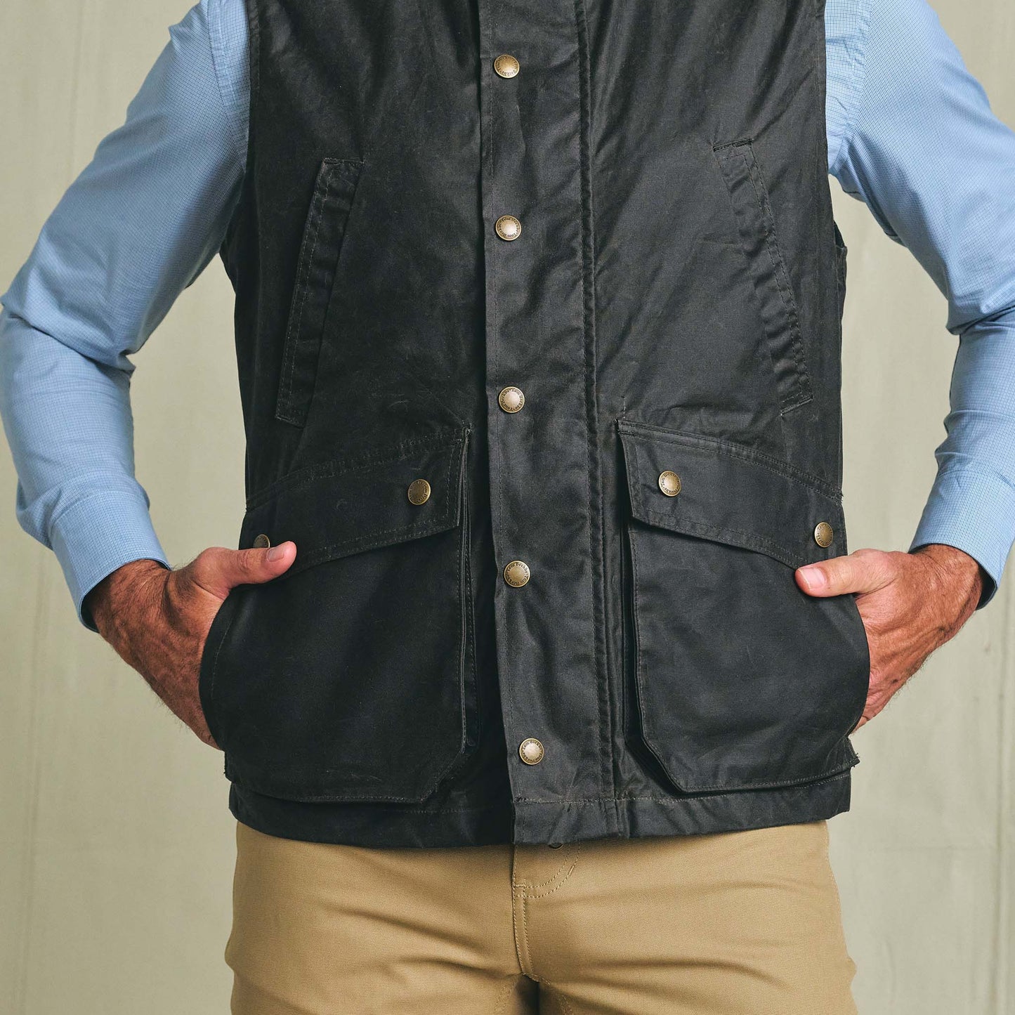 Person wearing the Tom Beckbe Kinsman Vest over a light blue shirt and tan pants, hands in vest pockets.
