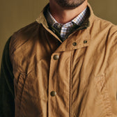Man wearing the Tom Beckbe Kinsman Vest in tan over a green shirt and checked button-down, shown shoulders to chin.