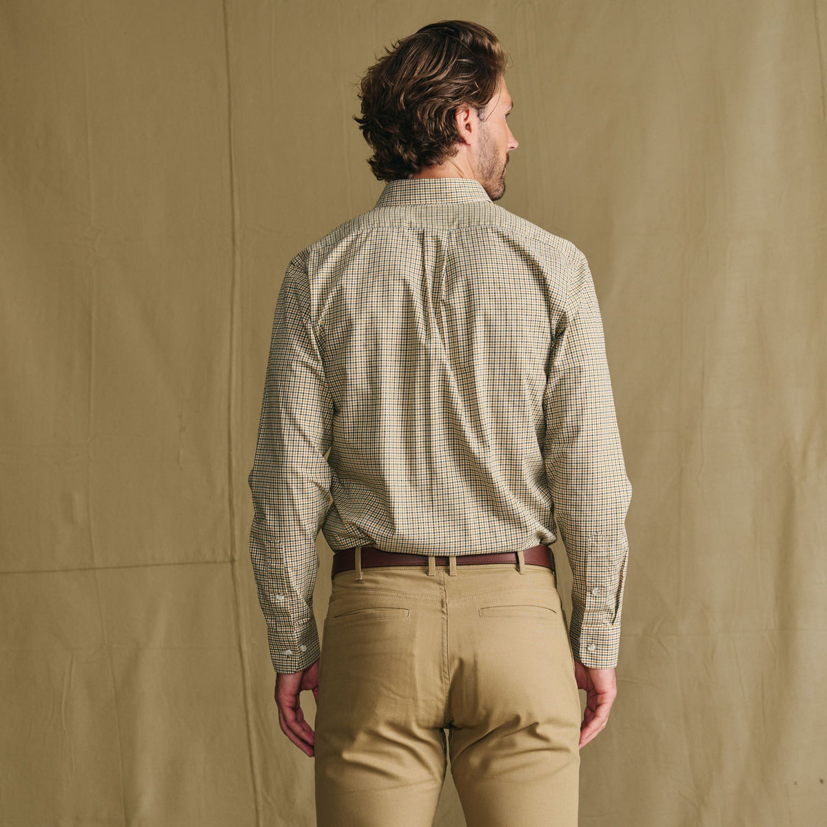 Man wears a Tom Beckbe Knapp Cotton Twill Shirt and tan pants, standing with his back to a tan background.