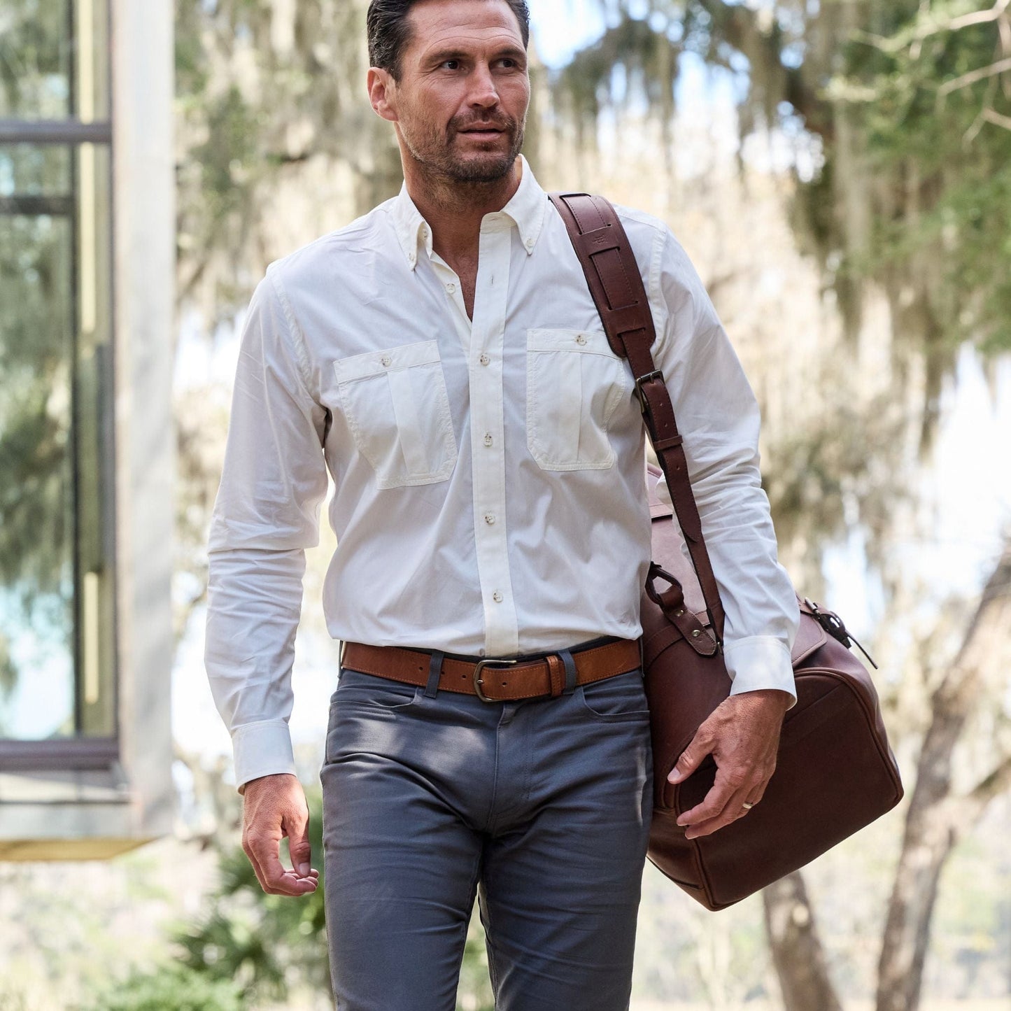 Man in white shirt, gray pants, carrying a Tom Beckbe brown bag with antique brass hardware.