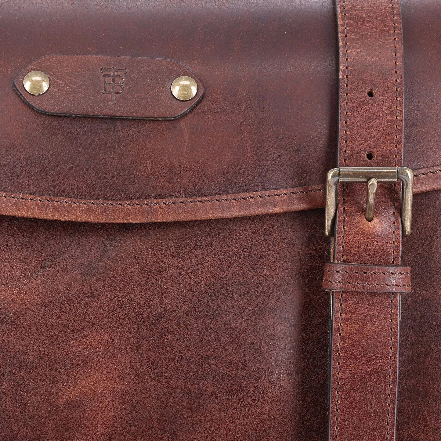 Close-up of a brown leather satchel with brass hardware and a visible embossed logo on the flap.