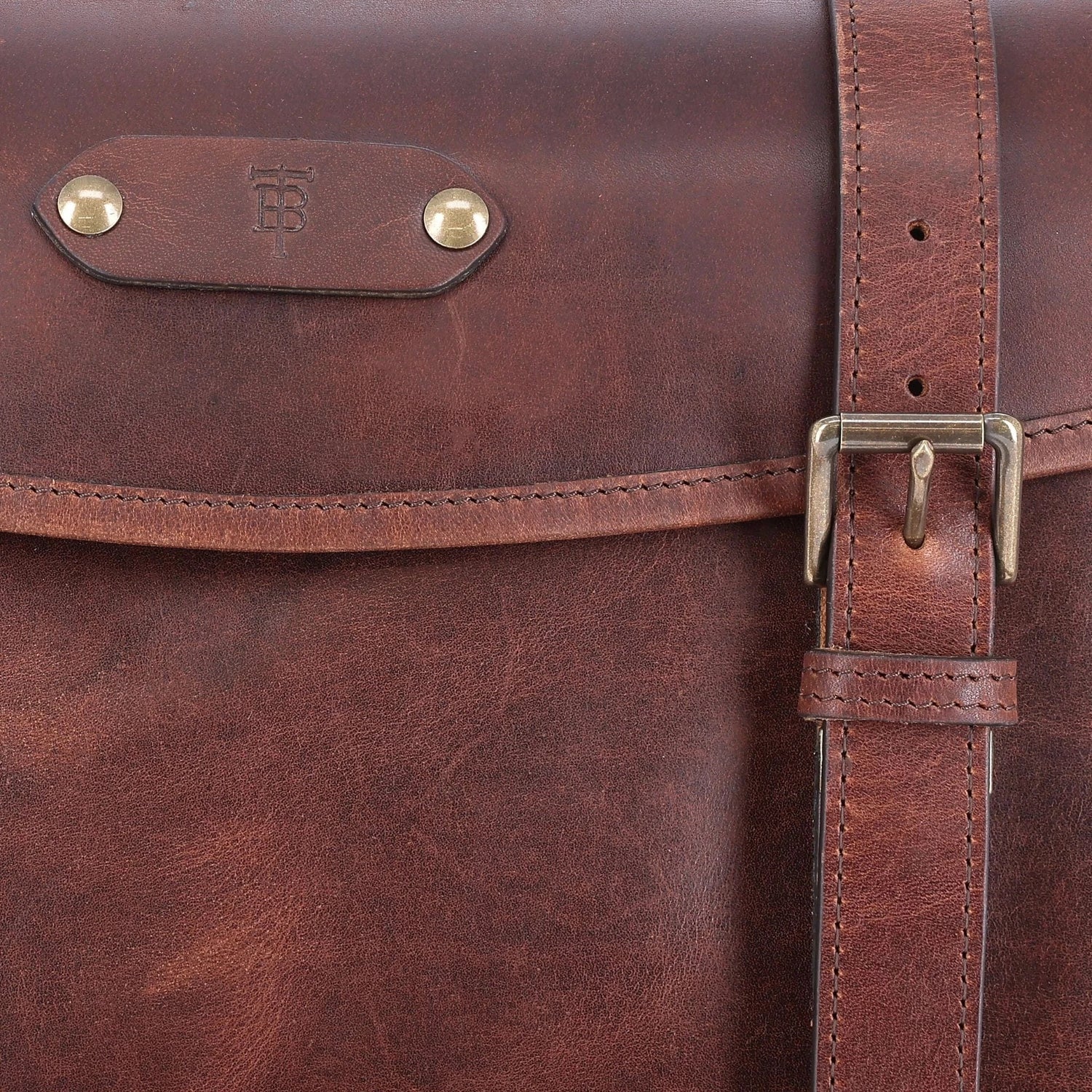 Close-up of a brown leather satchel with brass hardware and a visible embossed logo on the flap.