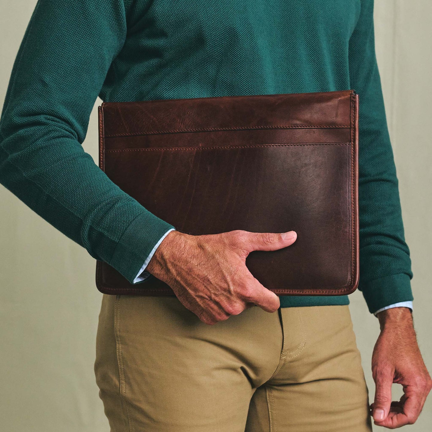 A person in a green sweater and tan pants carries the Tom Beckbe Leather Portfolio at their side.