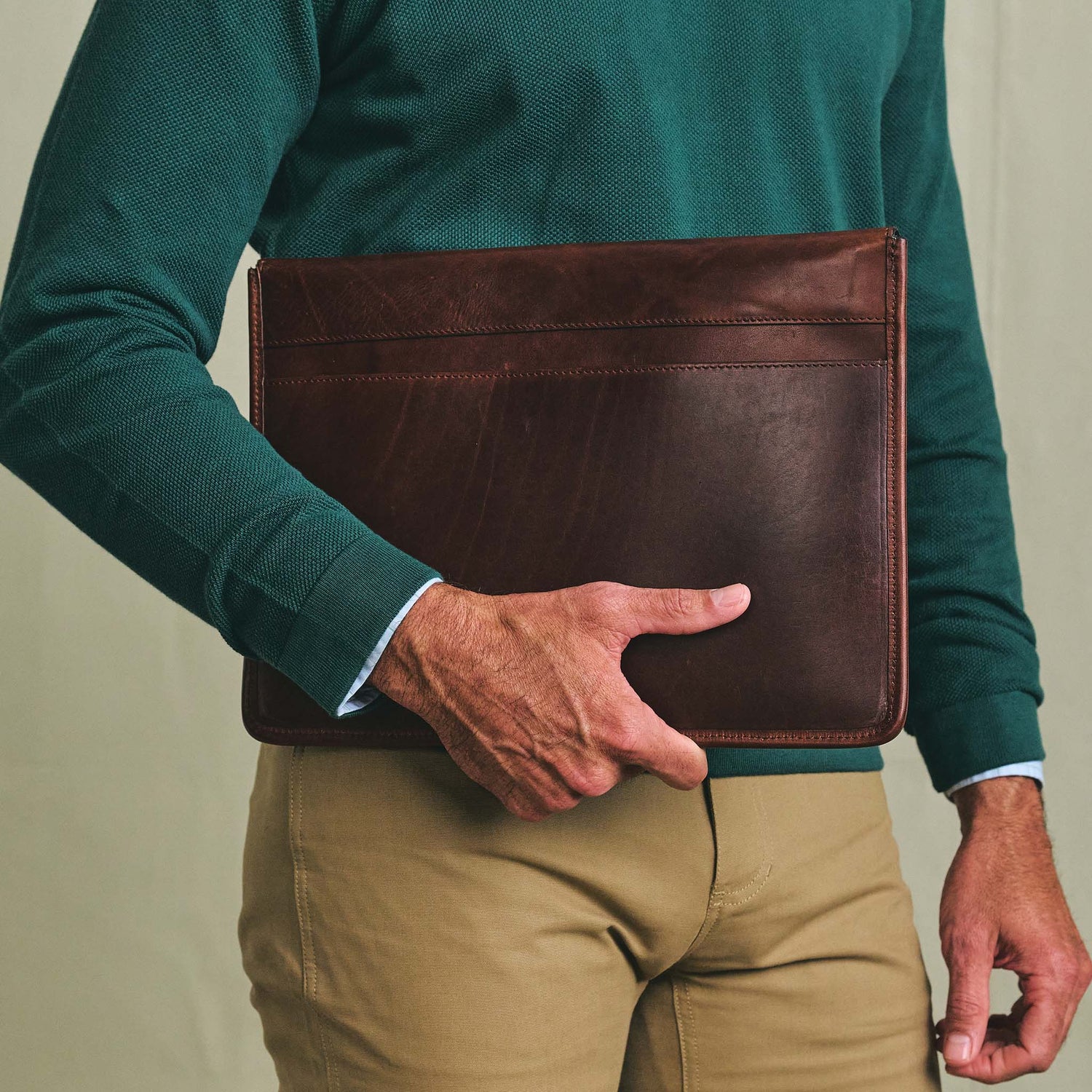 A person in a green sweater and tan pants carries the Tom Beckbe Leather Portfolio at their side.