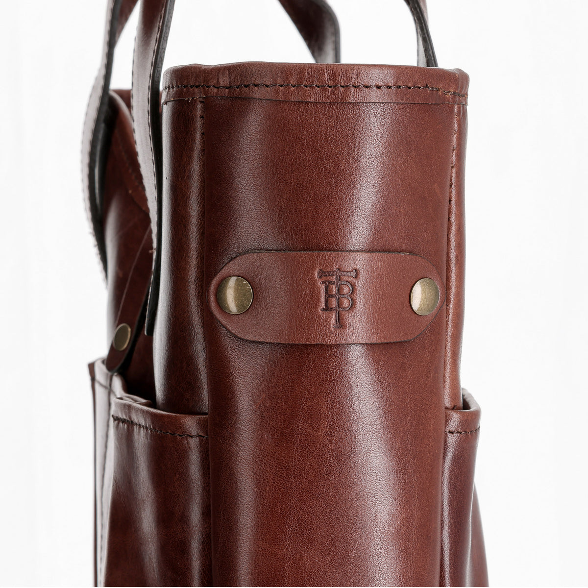 Close-up of the Tom Beckbe Leather Whiskey Tote with brass rivets and embossed initials on a white background.