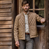 Man in vintage style, wearing a Logan Bomber Jacket by Tom Beckbe, leaning against a wooden buildings doorframe.