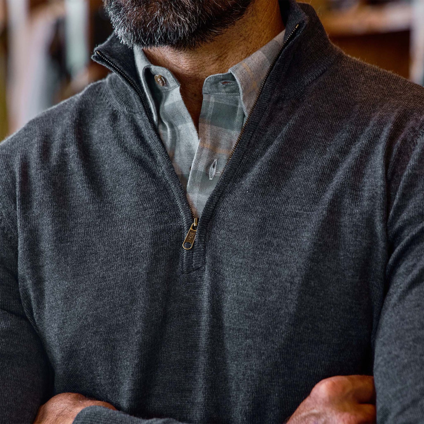 Bearded man wearing the Tom Beckbe York Merino Quarter Zip over a plaid shirt, arms crossed.