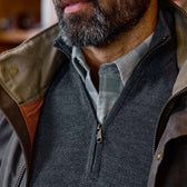 Close-up of a man in a plaid shirt and Tom Beckbe York Merino Quarter Zip layered under a brown jacket.
