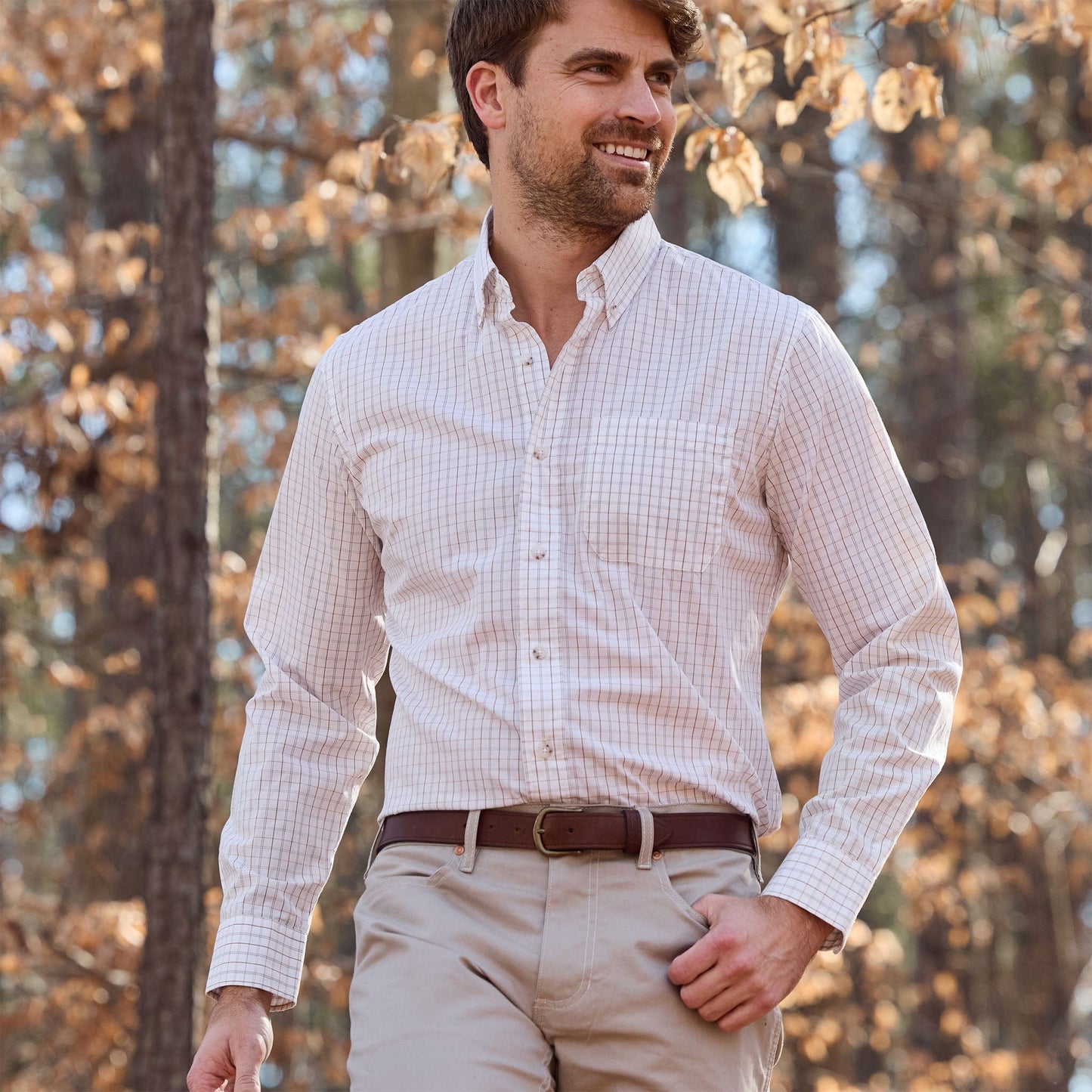 Man in Tom Beckbe Monroe Poplin Shirt and khaki pants walks outdoors among autumn trees.