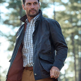 Man in a classic fit dark jacket and Tom Beckbes Monroe Poplin Shirt stands outdoors, trees in the background.