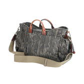 The Tom Beckbe Canvas Utility Bag in Mossy Oak Original Bottomland is shown with brown leather handles and a beige strap.
