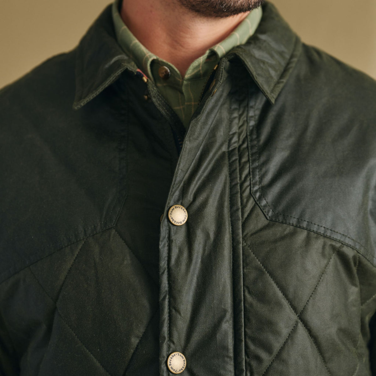 Close-up of a person in the Tom Beckbe Paddock Quilted Jacket over a green plaid shirt, face partially visible.