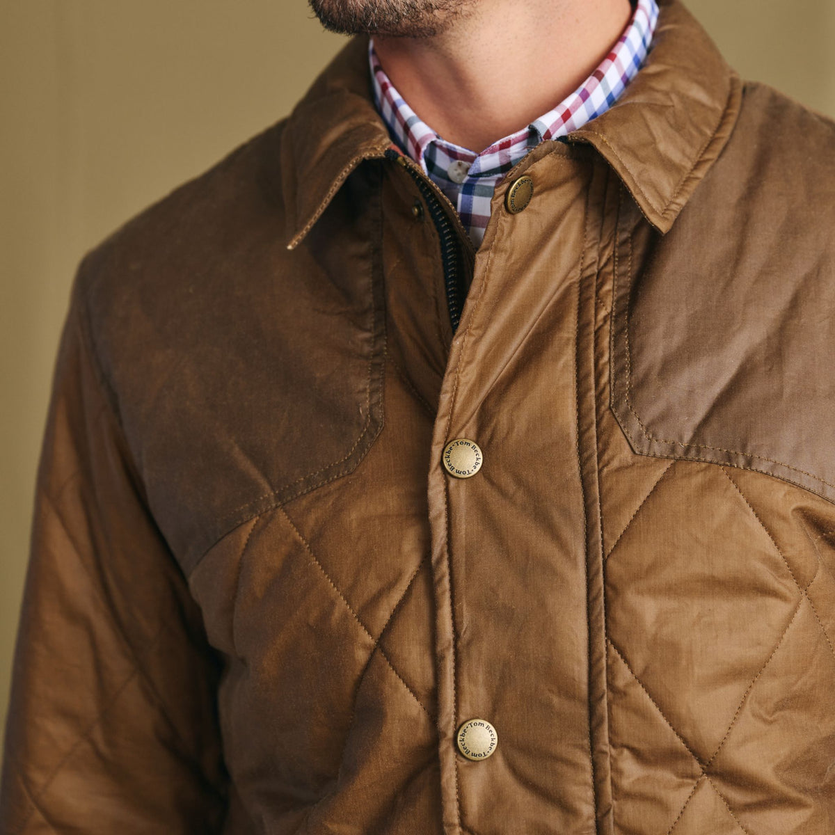 Man wearing Tom Beckbe Paddock Quilted Jacket over a checkered shirt; only upper torso and jacket visible.