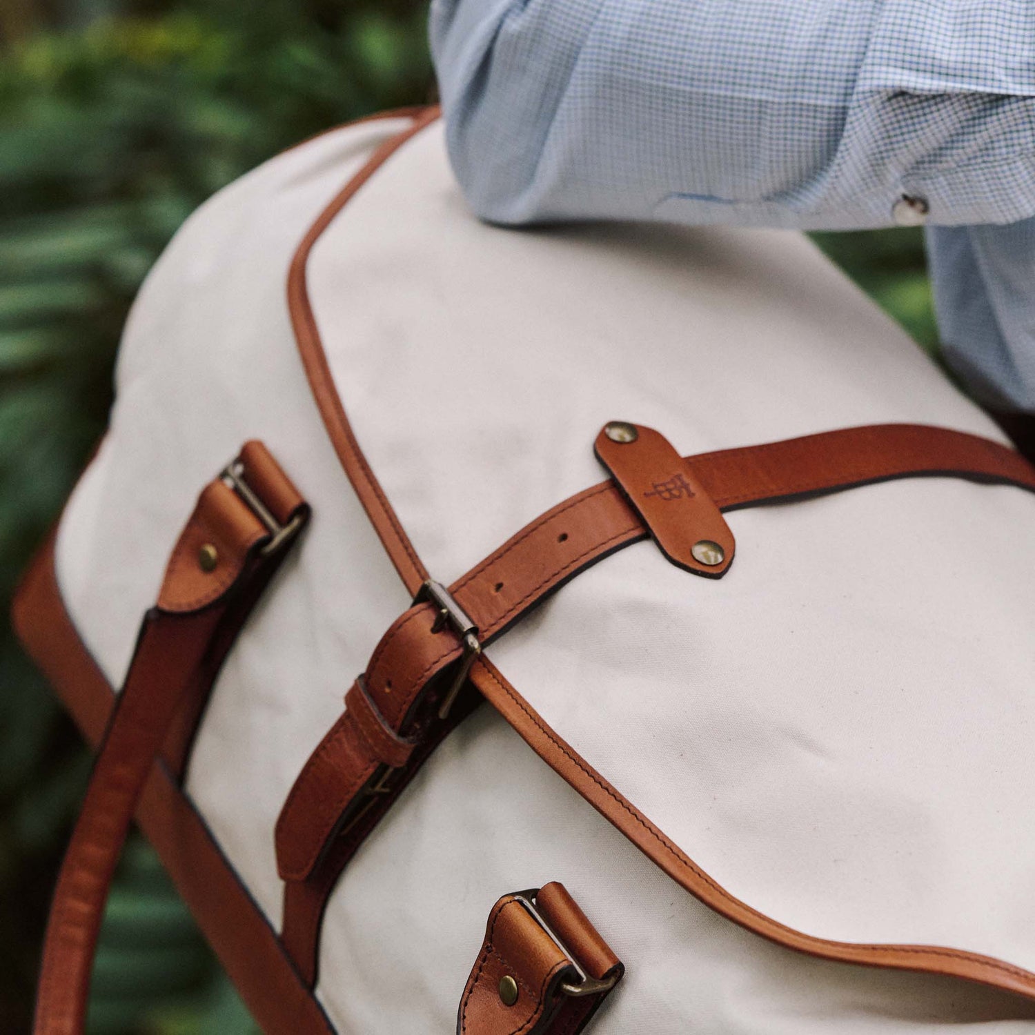 A person carries the Tom Beckbe Perdido Canvas Weekender Duffel Bag, wearing a light blue checkered shirt.