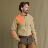 A man wears the Tom Beckbe Perry Field Shirt in beige with orange accents and two-tone brown pants, facing left.