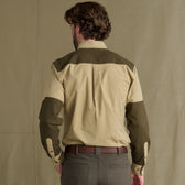 Man facing away, wearing a beige and olive Tom Beckbe Perry Field Shirt, gray trousers, against plain background.
