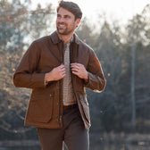 Man outdoors in a Tom Beckbe Piedmont Jacket over a plaid shirt, smiling with trees in the background.