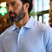 Man with a beard wearing a light blue polo shirt indoors, with blurred background.