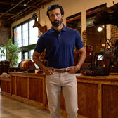 A man in a navy polo shirt and beige pants stands indoors in a store with wood counters and mounted animal heads on the walls.