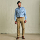 A man stands indoors wearing the Tom Beckbe Powell Performance Shirt, khaki pants, and brown dress shoes.